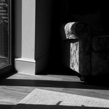 Find a black and white photograph of an armchair in the shadows. 