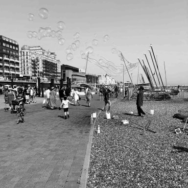 Find black and white photograph of man on beach making bubbles. 