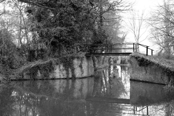 Find a black and white photograph of a canal with a bridge over it.