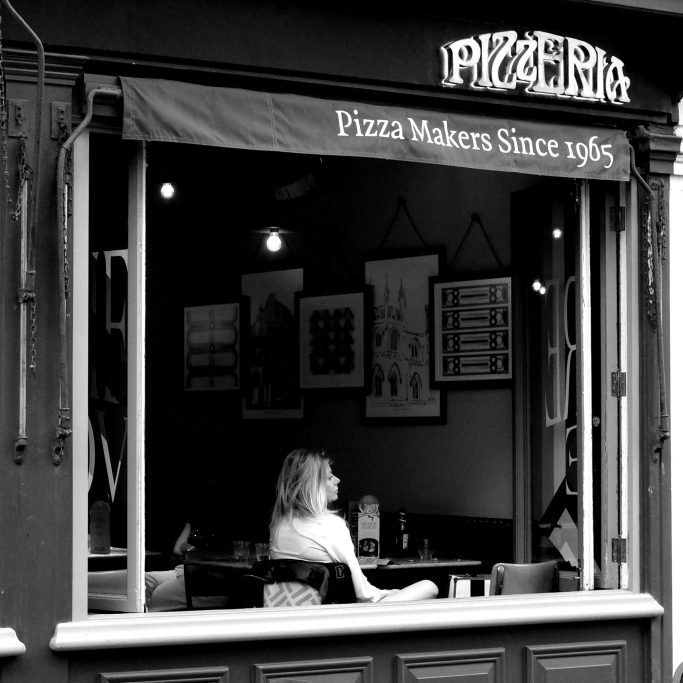 Waiting Black and white photograph of a young woman in a restaurant window.