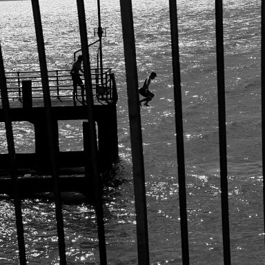 Find a black and white photograph of a boy jumping of a pier into the sea.